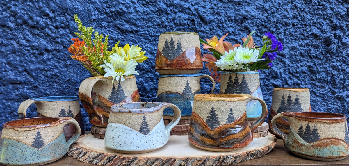 Set of ceramic mugs with nature-themed designs on a wooden surface against a blue wall.